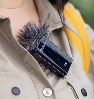 Clip-on wireless microphone with foam windscreen, attached to a light jacket