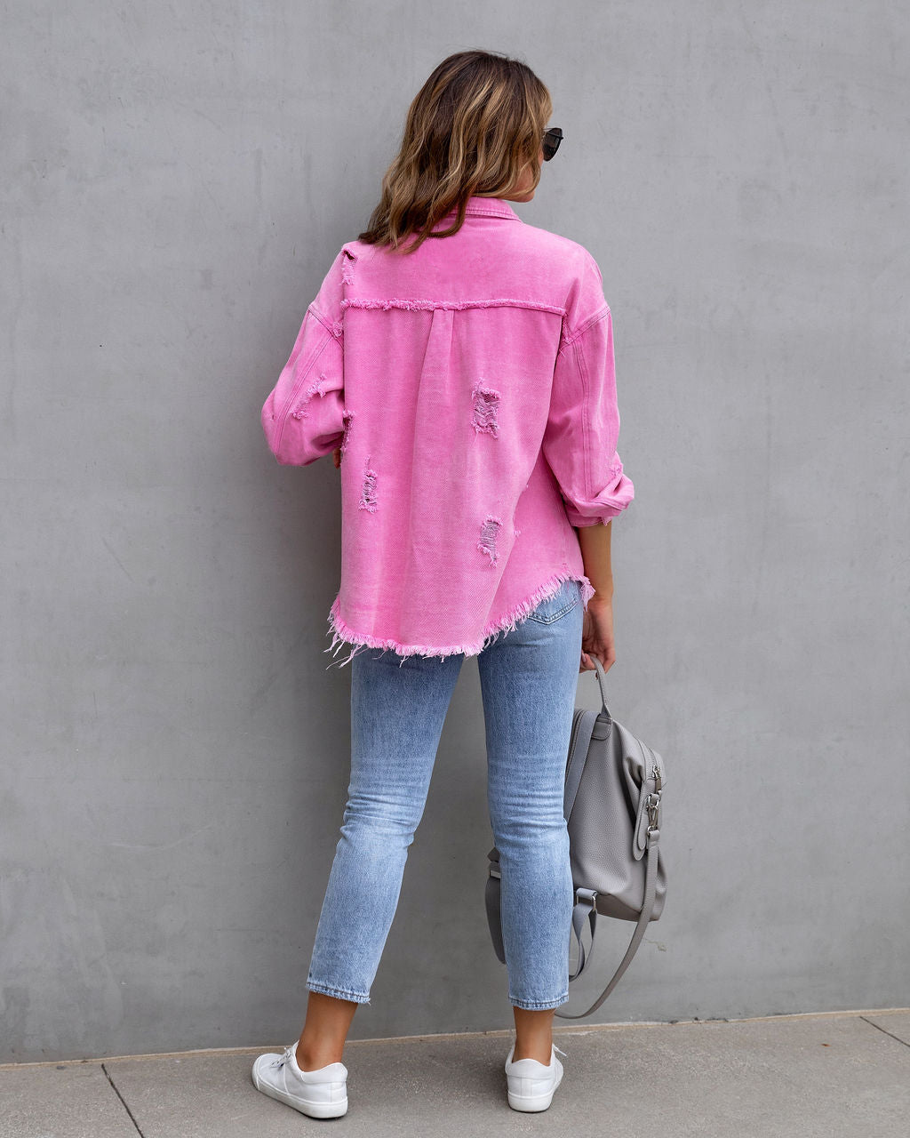 Women’s ripped denim shirt jacket in pink, shown from the back with button closure